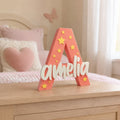 Stone Look Statues coral letter A nursery decor with white Amelia name and yellow star accents on a wooden dresser.