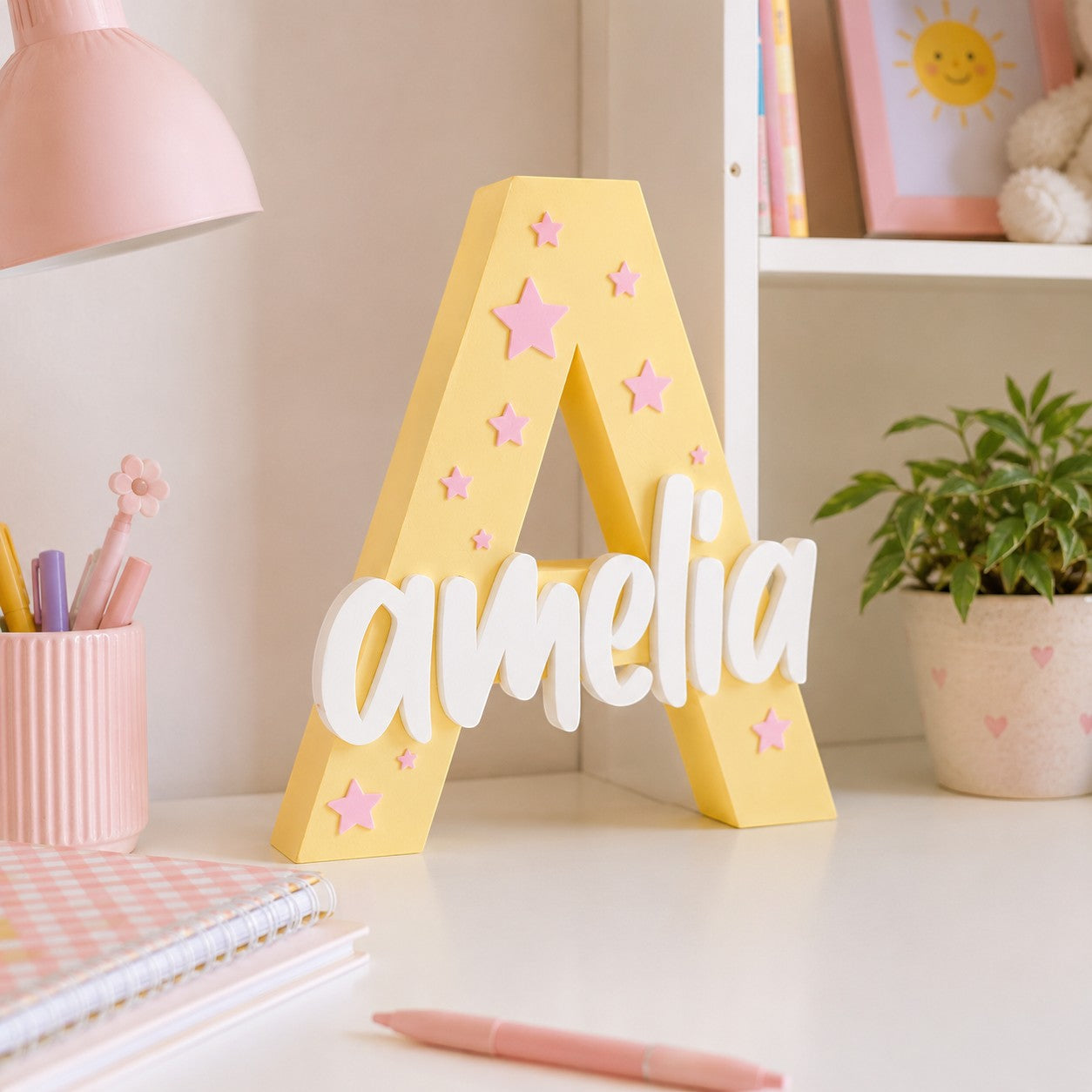 Stone Look Statues yellow letter A nursery decor with white Amelia name cutout and pink star accents on a desk.